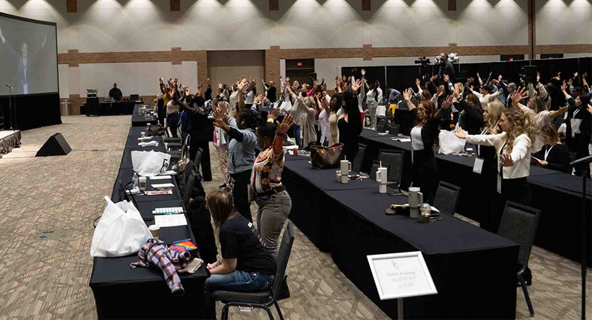 picture of both audience and presenter at the conference. Audience participating with hands held out. 